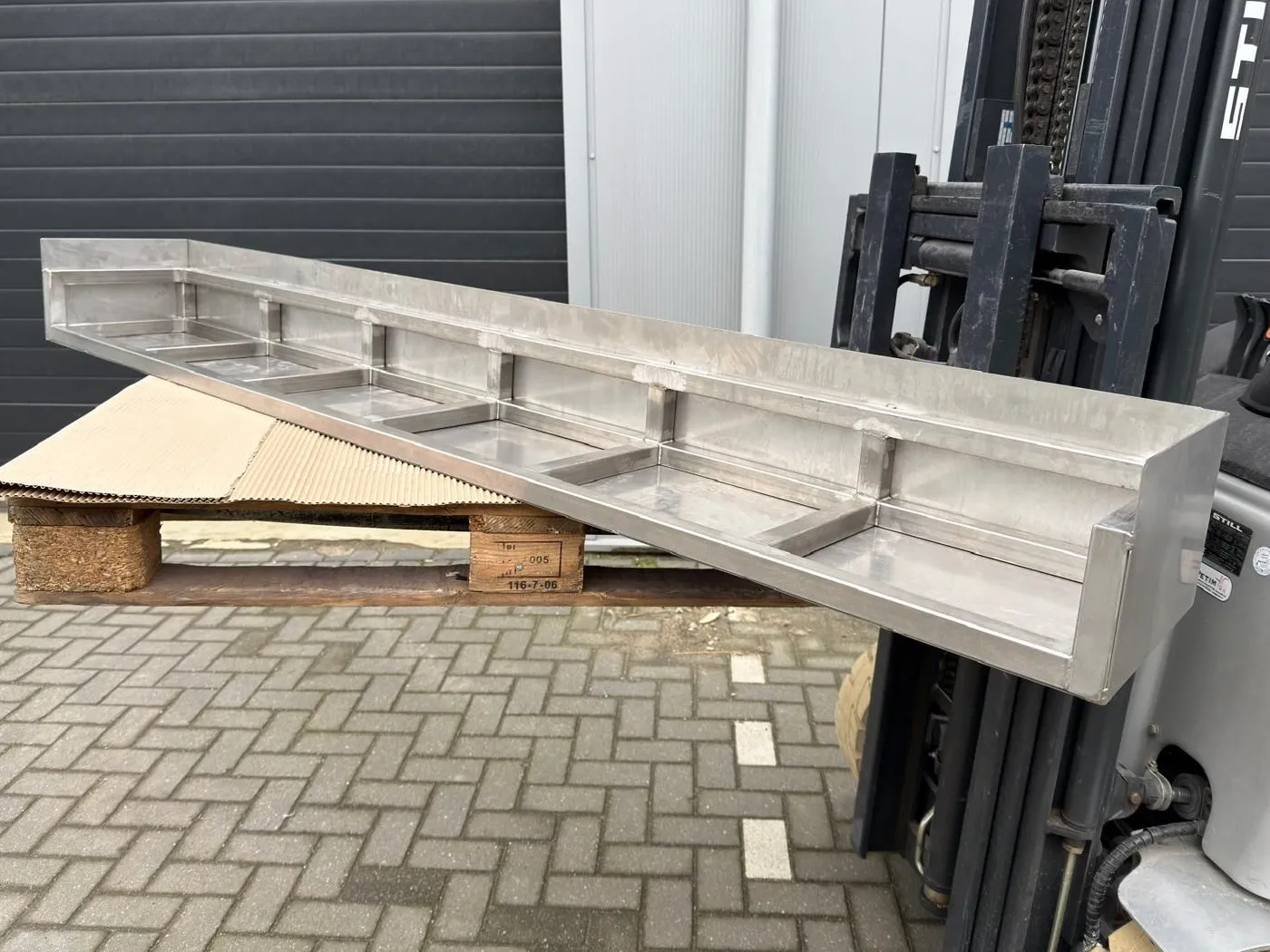 Lang gelast RVS-frame met vakken, op een pallet en de vorken van een heftruck